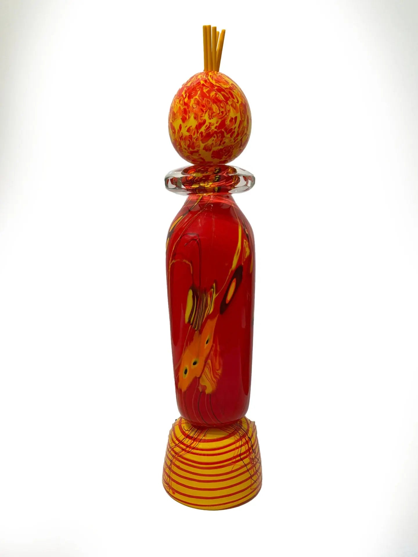 A vivid red glass sculpture titled "Red Inferno" by renowned American artist Steve Palmer features swirling yellow and orange accents, a decorative orb, and flame-colored spikes. Handblown with rich warm hues, it's a striking collector’s piece measuring 30 inches tall and weighing 20.7 lbs.