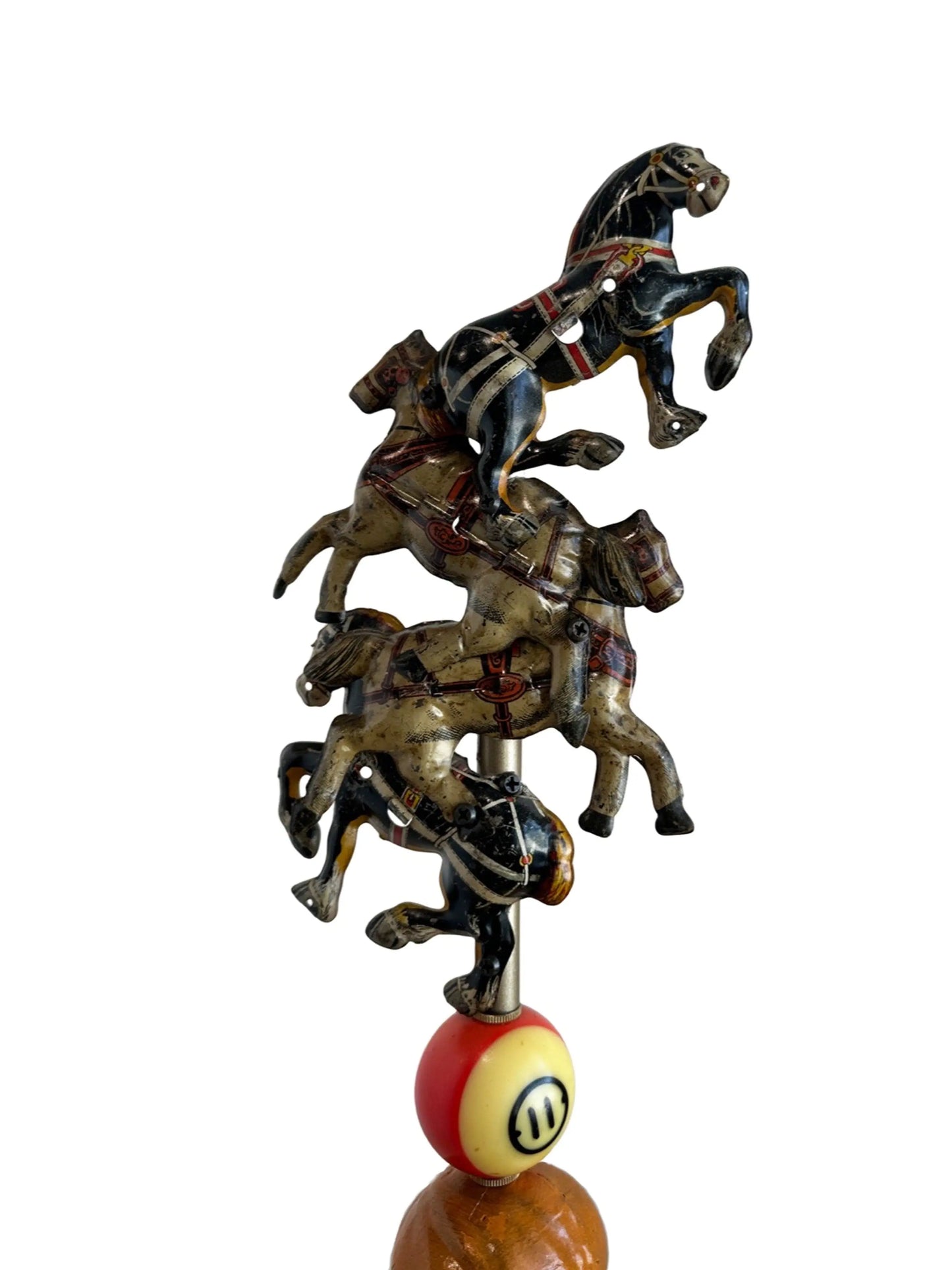 This sculpture, titled 'Skat Horses' by William Fink, is a whimsical standing piece made from vintage and antique components. It features a papier-mâché doll head with antique toy horses on top, a vintage Skat soap tin, a 1940s savings bank, a toy rabbit, and a spinning metal top, all arranged to evoke nostalgia and imagination. Measuring approximately 8.5 inches wide, 39 inches tall, and 8.5 inches deep, this mixed media artwork celebrates creativity through its playful use of found objects.