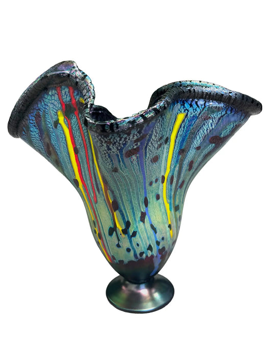 This vibrant, large molten organic vessel by Rick Hunter features a deep blue base with multicolored vertical drippings and an iridescent, shimmering rim in purple, green, and copper hues. Measuring approximately 12 inches in width and height, and weighing 2.82 pounds, this unique glass piece radiates energy and movement, showcasing bold colors and dynamic design in a one-of-a-kind artwork. 
