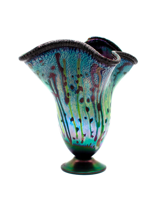 This vibrant, large molten organic vessel by Rick Hunter features a deep blue base with multicolored vertical drippings and an iridescent, shimmering rim in purple, green, and copper hues. Measuring approximately 12 inches in width and height, and weighing 2.82 pounds, this unique glass piece radiates energy and movement, showcasing bold colors and dynamic design in a one-of-a-kind artwork. 