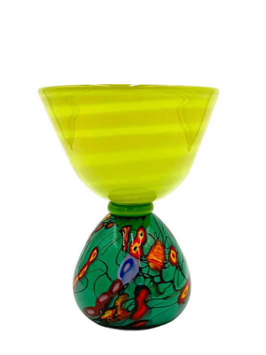 This vibrant glass sculpture, 'Mini Me' by Steve Palmer, showcases a bold abstract design with colorful swirls and organic patterns on a rounded base, contrasted by a translucent lime green top with subtle horizontal stripes. Its playful colors and shapes make it a striking statement piece suitable for contemporary and artistic settings. Dimensions are approximately 7 inches wide, 9 inches high, and 4.5 inches deep, weighing 4.4 pounds, and it is crafted from handblown glass.