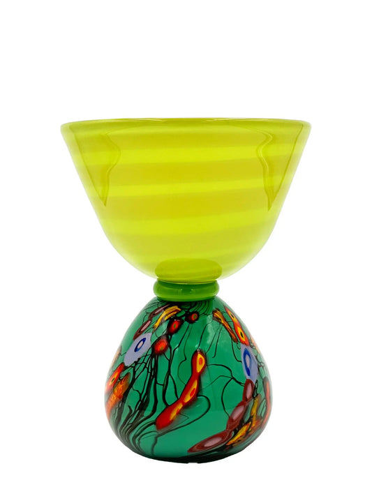 This vibrant glass sculpture, 'Mini Me' by Steve Palmer, showcases a bold abstract design with colorful swirls and organic patterns on a rounded base, contrasted by a translucent lime green top with subtle horizontal stripes. Its playful colors and shapes make it a striking statement piece suitable for contemporary and artistic settings. Dimensions are approximately 7 inches wide, 9 inches high, and 4.5 inches deep, weighing 4.4 pounds, and it is crafted from handblown glass.
