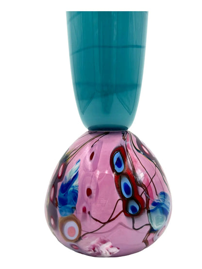 This glass art piece titled 'Cotton Candy' by Steve Palmer features a sleek turquoise body with a vibrant swirl of purple, pink, and blue at the base, blending contemporary design with craftsmanship. It can serve as a sculpture or functional vase, measuring 3" wide, 15" high, and weighing 3.7 lbs.