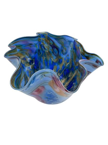 Ocean Song by Steve Palmer is a handcrafted glass bowl inspired by underwater life, featuring ruffled edges and a sky-blue base with vibrant abstract red, orange, pink, and deep blue patterns, conveying movement and energy. Measures approximately 13" wide, 9" high, and weighs 6.15 lbs.