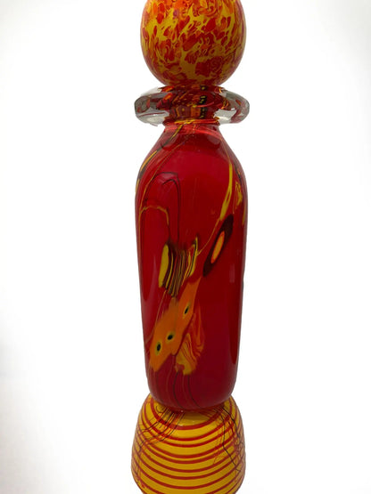 A vivid red glass sculpture titled "Red Inferno" by renowned American artist Steve Palmer features swirling yellow and orange accents, a decorative orb, and flame-colored spikes. Handblown with rich warm hues, it's a striking collector’s piece measuring 30 inches tall and weighing 20.7 lbs.