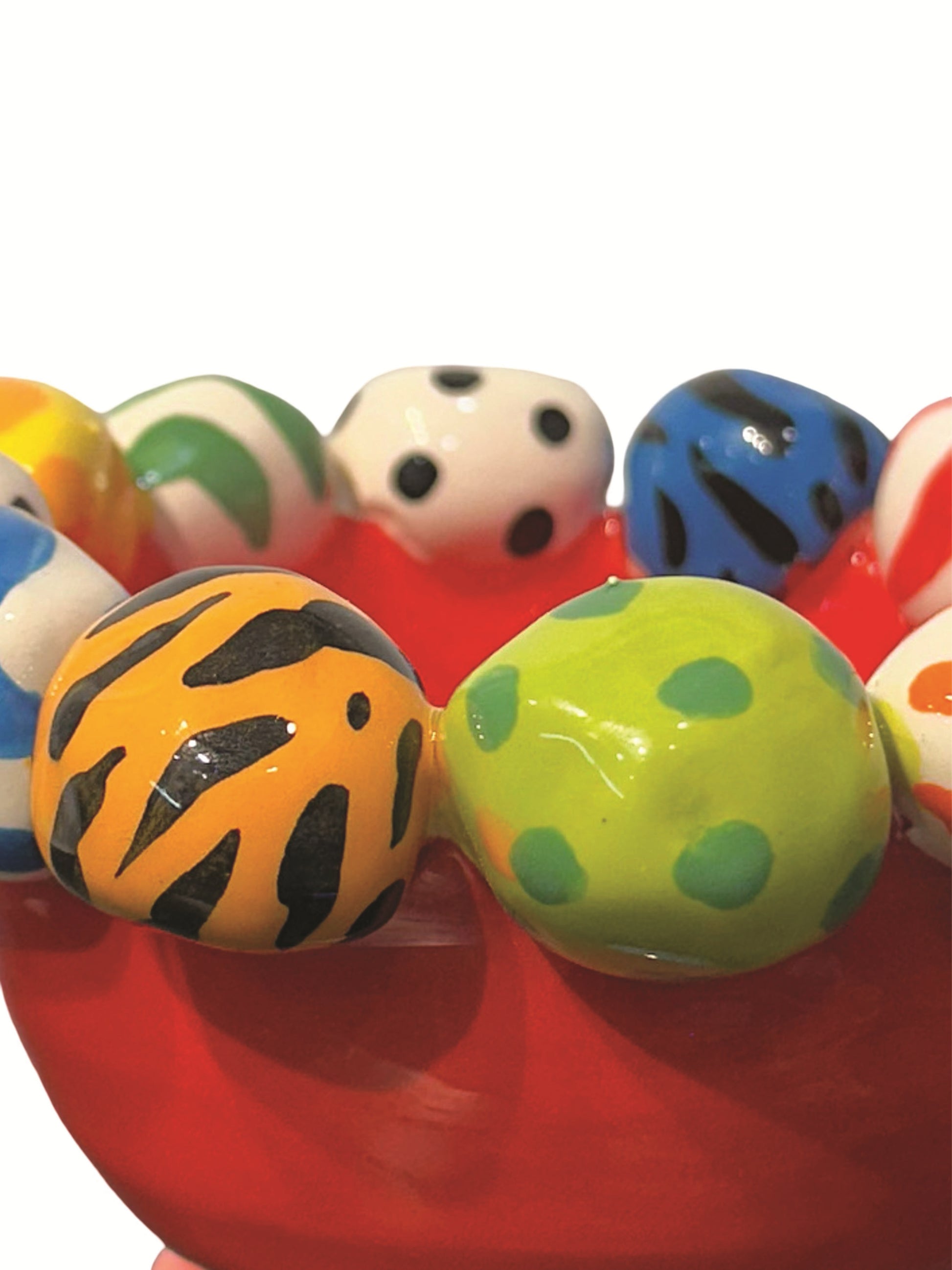 A Mary Rose Young handmade ceramic footed bowl featuring a bold red glaze, topped with a rim of hand-painted orbs in playful stripes, polka dots, and animal prints. Resting on sculpted blue, pink, and gold feet, this striking statement piece is perfect for both serving and décor. Dimensions are approximately 6.5 inches in width and depth, and 4 inches in height. 