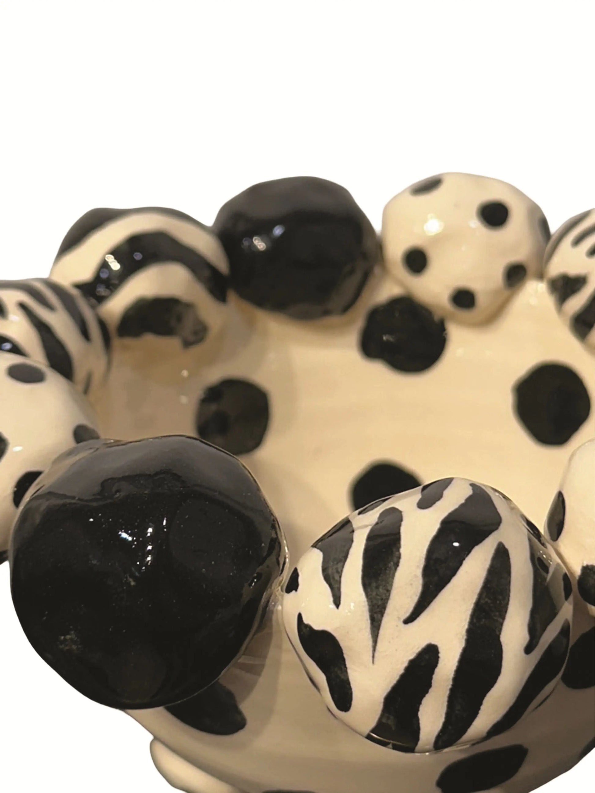 This handmade ceramic footed bowl, designed by Mary Rose Young, features a bold black and cream pattern with hand-painted dots, zebra stripes, and solid black accents. The sculpted dotted feet complement the playful rim, adding charm and balance. Measuring approximately 8 inches wide, 8 inches deep, and 5 inches high, this striking piece serves as both a functional bowl and a decorative statement, perfect for enhancing any table, shelf, or display with artistic flair.