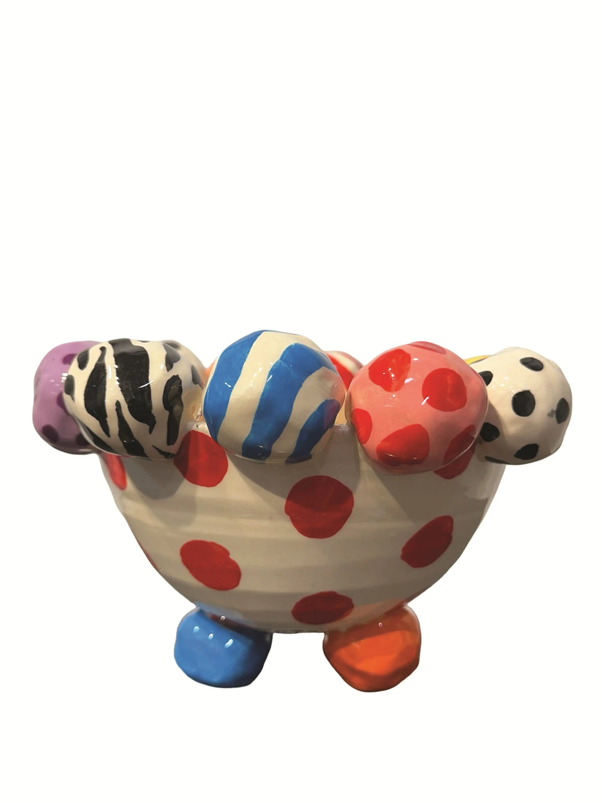 This handmade ceramic-footed bowl by Mary Rose Young features a whimsical design with a creamy white base decorated with bold red polka dots. The rim is adorned with hand-painted orbs displaying various patterns such as zebra stripes, colorful swirls, and polka dots. Resting on sculpted orange, blue, and gold feet, this vibrant piece is ideal for serving or decorative use, measuring approximately 8.5 inches in width and depth and 5.5 inches tall.
